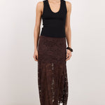 A woman modeling a sleeveless black ribbed tank top and a dark brown lace maxi skirt, styled with black sunglasses and flat sandals, against a plain white studio background.