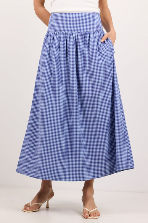 A model wearing a blue and white gingham pleated midi skirt with side pockets, paired with a white top and beige heeled sandals, against a plain white studio background.