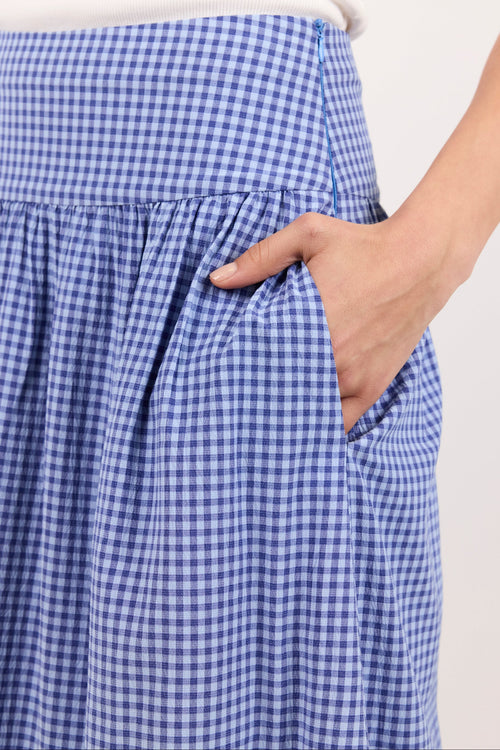 Close-up of a person wearing a blue and white gingham skirt with a side pocket, holding the pocket with one hand.