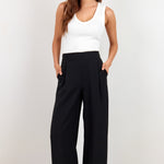A woman modeling a white sleeveless tank top and black wide-leg trousers against a plain white studio background.