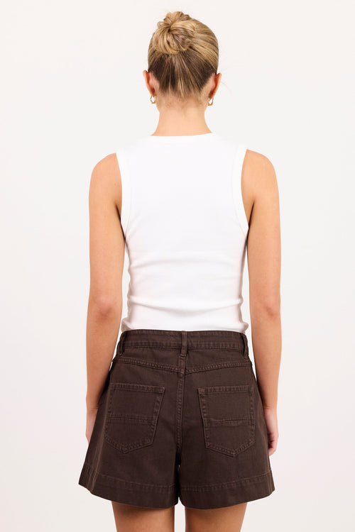 A woman viewed from behind wearing a white sleeveless top and dark brown shorts against a plain white studio background.