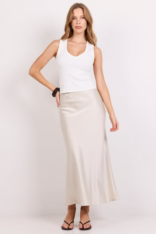 A woman modeling a white sleeveless tank top and a long, flowing cream satin midi skirt against a plain white studio background.