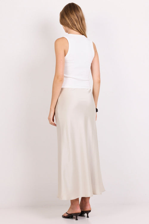 A woman shown from the back wearing a white sleeveless top and a long cream-colored satin skirt, paired with black heels, against a plain white studio background.