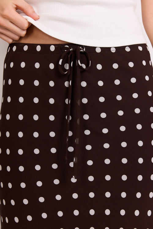 A close-up of a person wearing a black skirt with a white polka dot pattern and a matching black drawstring waist, paired with a white top.