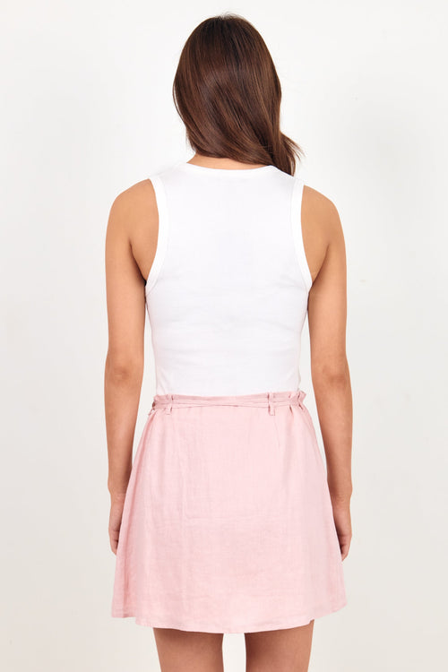 A woman viewed from behind wearing a white sleeveless top and a light pink flared skirt against a plain off-white studio background.