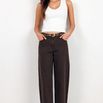 A woman modeling dark brown wide-leg cropped pants with a black belt, paired with a white tank top and black sandals, standing against a plain white studio background.