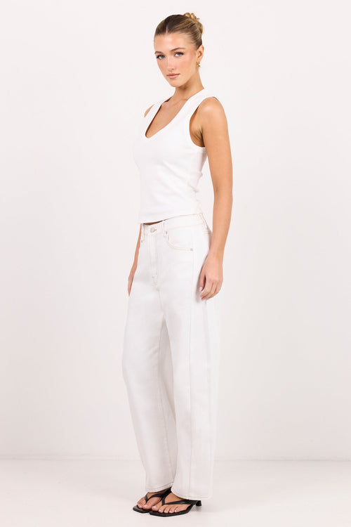 A woman modeling a white sleeveless crop top and white wide-leg jeans against a plain white studio background.
