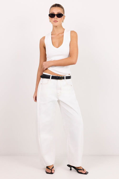 A model wearing a white sleeveless top, white wide-leg jeans with a black belt, black sandals, and sunglasses, standing against a plain white studio background.