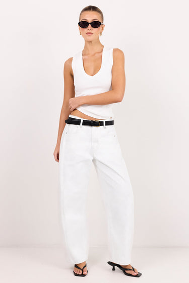 A model wearing a white sleeveless crop top, white wide-leg jeans, a black belt, and black sandals, standing against a plain white studio background.