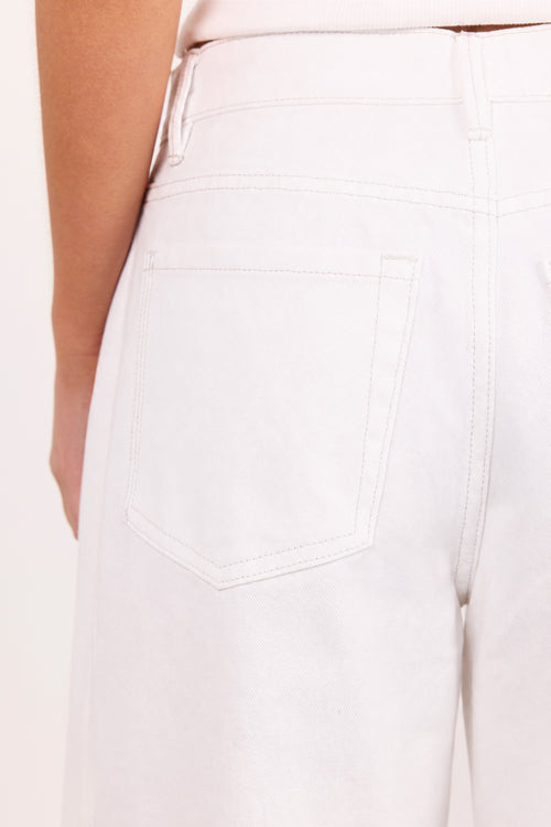 Close-up of the back waistband and pocket area of light-colored pants worn by a model, showing part of the arm and torso against a plain light background.