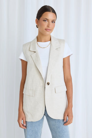 Model wears a beige linen vest, a white top and blue jeans