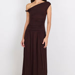 A woman modeling a dark brown one-shoulder midi dress with a gathered bodice and flowing skirt, standing against a plain white studio background.