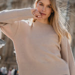 Woman in a beige sweater standing in front of a classical building