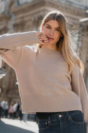 Woman in a beige sweater standing in front of a classical building