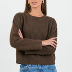 Woman wearing a brown sweater and blue jeans on a white background
