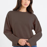 Woman wearing a brown sweater and blue jeans on a white background