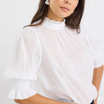 woman wearing a relaxed ivory short sleeve top with frilled neckline and sleeves, paired with indigo jeans.