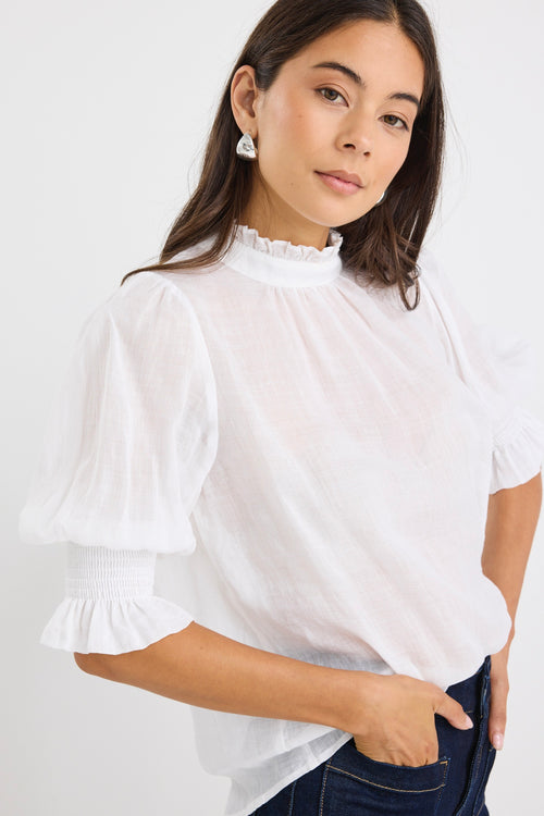 woman wearing a relaxed ivory short sleeve top with frilled neckline and sleeves, paired with indigo jeans.