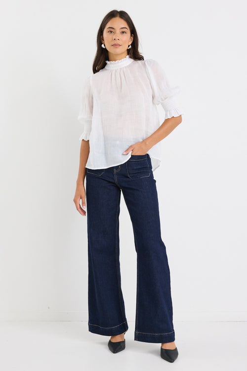 woman wearing a relaxed ivory short sleeve top with frilled neckline and sleeves, paired with indigo jeans.