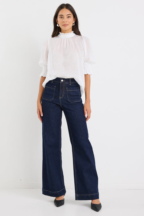 woman wearing a relaxed ivory short sleeve top with frilled neckline and sleeves, paired with indigo jeans.
