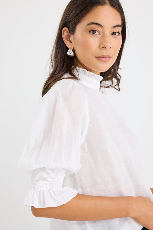 woman wearing a relaxed ivory short sleeve top with frilled neckline and sleeves, paired with indigo jeans.