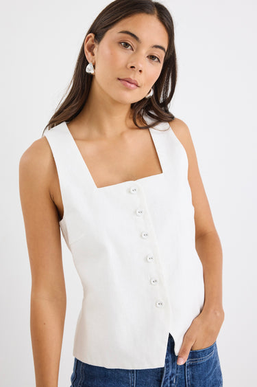 Woman wearing an ivory sleeveless linen vest with an off-centre button-down front, styled with blue jeans.