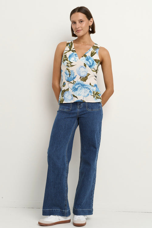 Woman wearing a sleeveless V-neck top with a vintage blue floral print, styled with blue high-waisted jeans.
