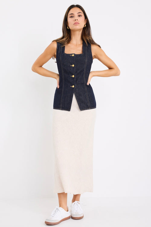 model wears a dark blue denim vest with a beige linen midi skirt