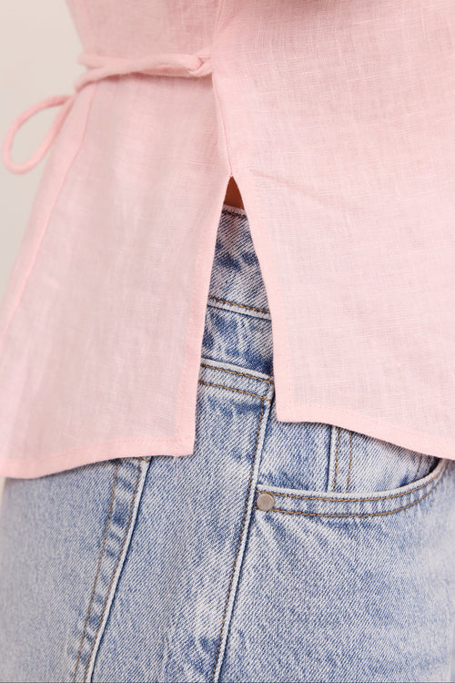 Close-up of a person wearing a light pink sleeveless top with a side tie and front slit, paired with light blue denim jeans.