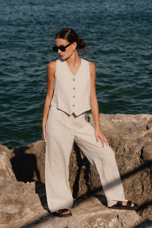 model wears a matching natural linen vest and pants combo at the beach