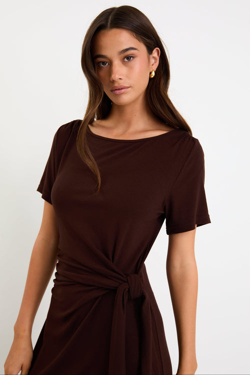 Model wearing a chocolate brown short sleeve jersey maxi dress with a waist tie and side split