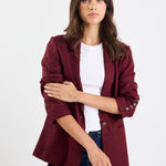 Woman wearing a burgundy blazer over a white shirt and blue jeans on a white background