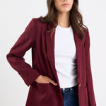 Woman wearing a burgundy blazer over a white shirt and blue jeans on a white background