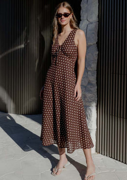 Woman in a brown polka dot dress standing against a textured wall.