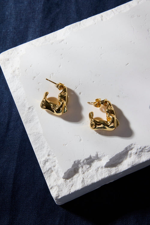 Gold earrings on a white stone surface with a dark background
