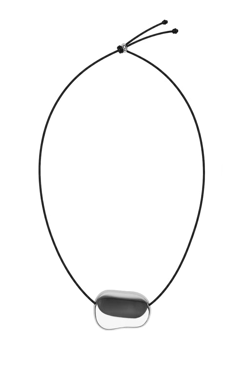 A minimalist black cord necklace featuring a smooth, irregular-shaped dark gray stone pendant set in a polished silver bezel, shown against a solid white background.