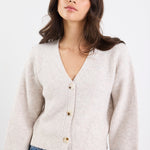 Woman wearing a beige ribbed sweater and blue jeans against a white background