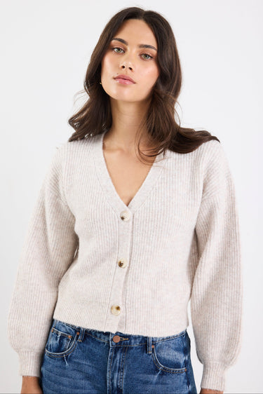 Woman wearing a beige ribbed sweater and blue jeans against a white background