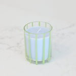 A white candle in a clear glass holder with light green vertical stripes, set on a white marble surface against a white background.