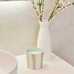 A bathroom vanity scene with a white ceramic vessel holding delicate flowering branches, next to a small striped soap dish on a white countertop.