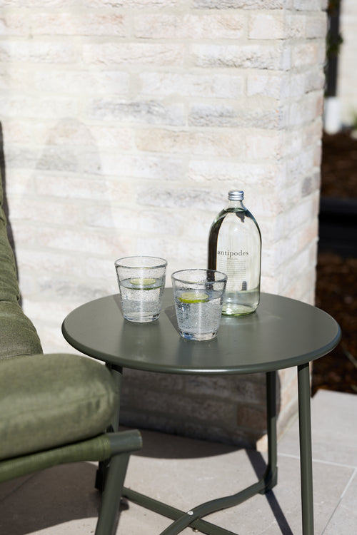 Two clear handmade bubble glass tumblers styled on a sage green outdoor side table.