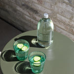 Two green handmade bubble glass tumblers with cucumber garnish styled on a sage green table.