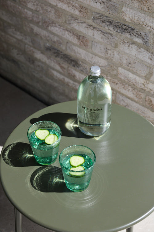 Two green handmade bubble glass tumblers with cucumber garnish styled on a sage green table.