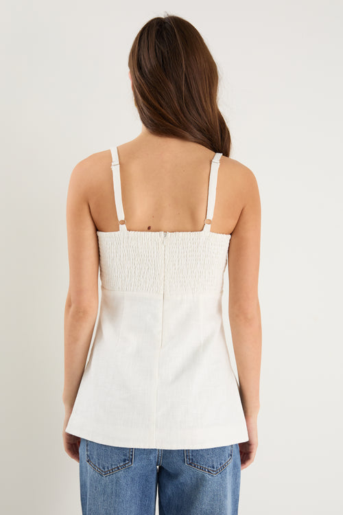 Woman wearing a fitted ivory vest top with thin straps, front buttons, and a clean, tailored silhouette.