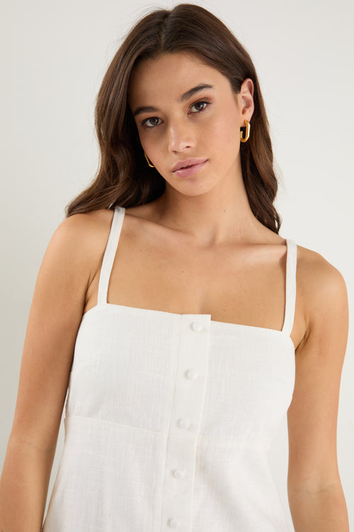 Woman wearing a fitted ivory vest top with thin straps, front buttons, and a clean, tailored silhouette.