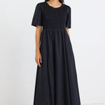 Woman wearing a black midi dress with shirred bodice and short puff sleeves, styled with black sneakers and gold earrings.