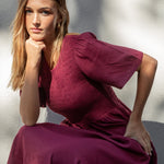 Woman in a burgundy dress sitting on the ground with a blurred background