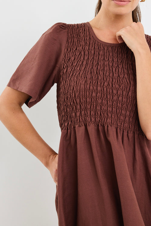 Model wears brown midi dress with a shirred cotton bodice and short sleeves