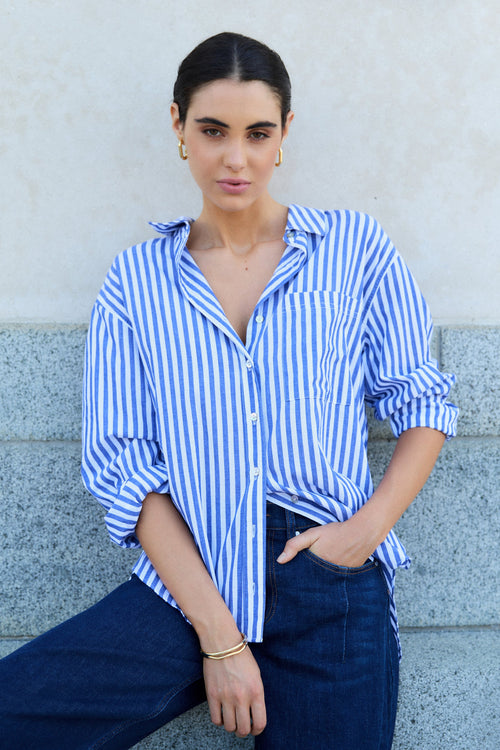 Woman wearing a blue and white striped shirt and dark jeans against a light-colored wall.