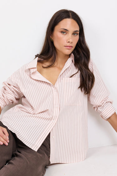 Woman wearing a light pink striped shirt and brown pants on a white background